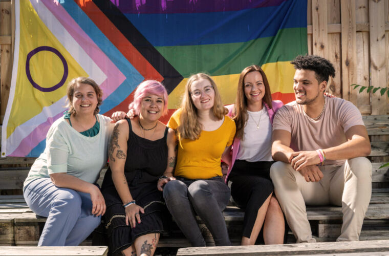 Fünf Accsonaut:innen sitzen im Innenhof des Darmstädter Accso Büros vor der Diversity Flagge