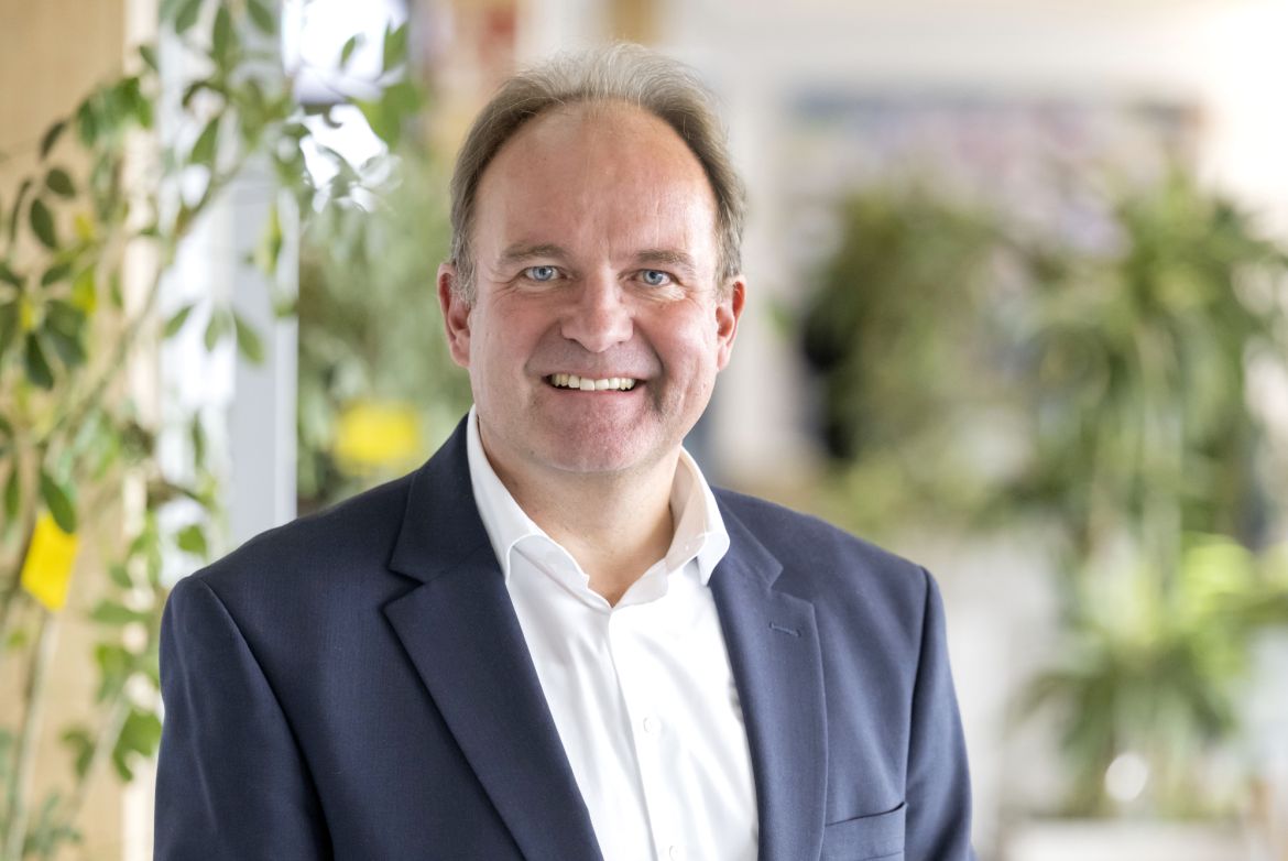 Dr. Haller mit blauem Blazer und weißem Hemd in die Kamera lächelnd.