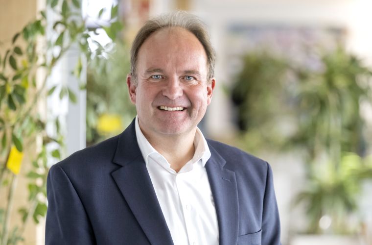 Dr. Haller mit blauem Blazer und weißem Hemd in die Kamera lächelnd.