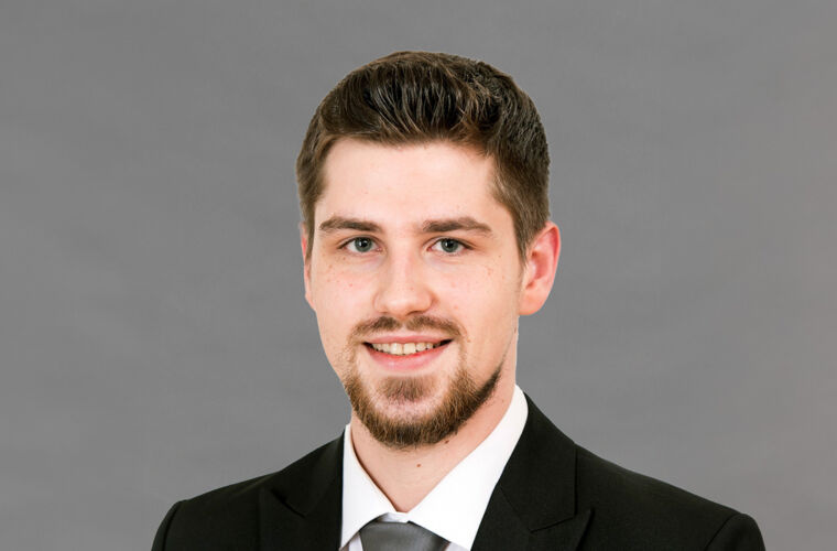 Marcel Aniol in die Kamera blickend, mit dunklem Anzug und Krawatte.