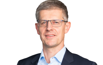 Porträt einer Person mittleren Alters mit kurzen grauen Haaren, Brille, hellblauem Hemd und dunklem Anzug; leichtes Lächeln.