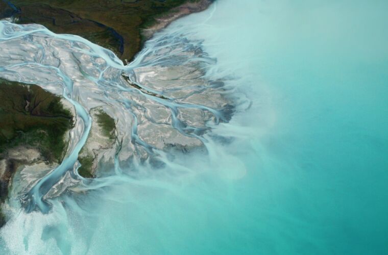 Zu sehen ist ein Flussdelta, welches mit vielen Verzweigungen in einem klaren türkisblauen See mündet.