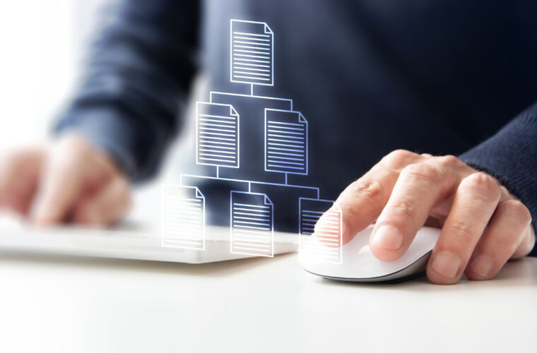 Eine Person arbeitet an einem Computer mit einer Hand auf einer Maus. Über der Hand schwebt ein holografisches Diagramm, das ein Dateisystem oder eine Dokumentenstruktur darstellt, bestehend aus mehreren miteinander verbundenen Dokumentensymbolen. Die Szene symbolisiert digitale Organisation und Datenmanagement.